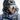 A person in a climbing helmet, Julbo Eyewear Edge Cover sunglasses, a blue insulated jacket, and a backpack looks to the side in a snowy outdoor setting.