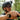 A close-up lifestyle shot of a man mountain biking in a forest, wearing a black Specialized helmet, black sunglasses, and a dark gray jersey, holding a black handlebar.