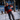 A man wearing Julbo-usa Cham mirror lenses and a red-blue jacket skis cross-country on a snowy trail, with trees and another skier in the background—an alpine classic.