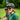 A person in a green shirt smiles outdoors wearing Julbo Eyewear's Density sunglasses with CustomFit Temples and a bike helmet, while another cyclist is blurred in the background.
