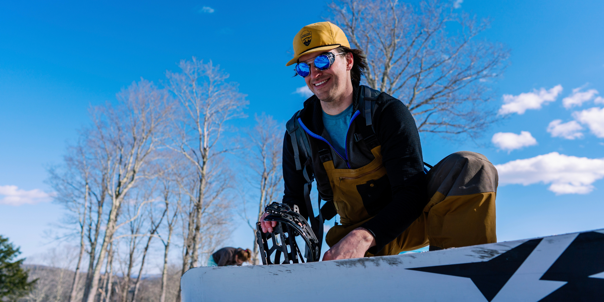 Snowboarder adjusting bindings with Legacy sunglasses on