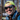 A man in a neon yellow cap and Julbo-usa Explorer 2.0 glacier sunglasses smiles outdoors, wearing a denim jacket and backpack with blurred trees in the background.