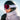 A person wearing a black ski helmet, Julbo Eyewear Cyrius X red ski goggles with anti-fog photochromic lens, black gloves, and a light jacket stands outdoors in snow.