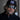 A man with curly hair, a beard, and mustache wears a black cap, dark zip-up jacket, and Julbo Eyewear Density Black Series performance sunglasses with large Black Spectron 3 lenses, looking directly at the camera.