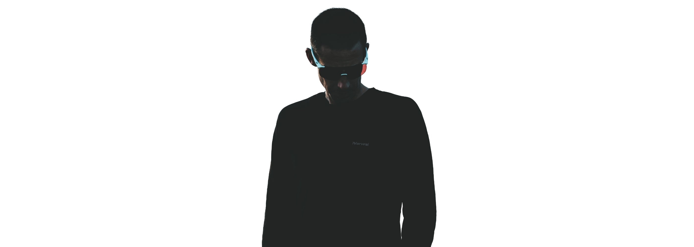 A person in a dark long-sleeve shirt stands against a white background wearing futuristic glowing glasses, with their face partially obscured by shadows.