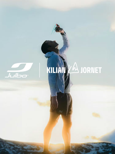 A person stands outdoors on rocky terrain, drinking from a soft flask, with sunset light behind. Logos for Julbo and Kilian Jornet are overlaid on the image.