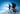 Two skiers wearing helmets and goggles carry skis while walking uphill on a snowy slope under a clear blue sky.
