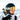 Person wearing a ski helmet and reflective goggles, carrying skis on their shoulder, standing outdoors with snow-covered mountains in the background.