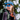 A woman smiles outdoors in a snowy forest, wearing Julbo Eyewear Legacy glacier glasses with leather side shields, a blue cap, and a backpack.