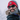 A man with a beard wearing a red beanie, sunglasses, and winter clothing smiles outdoors in snowy, windy weather.