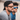 Two men outdoors wear Julbo-usa Renegade adventure sunglasses with casual shirts. The man in front has his cap backwards, while the other, slightly blurred in the background, enjoys wide-angle sun protection.