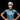 A cyclist in a blue jersey and white helmet stands with hands on hips, smiling, against a black background.