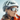 A woman wearing a white helmet and reflective sunglasses stands outdoors, dressed in an orange jacket, with snowy mountains visible in her lenses.