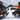 Two people in winter clothes sit on wooden chairs in snowy mountains, enjoying the view with Julbo-usa Shield M eyewear—featuring mountain-grade protection and removable side shields.