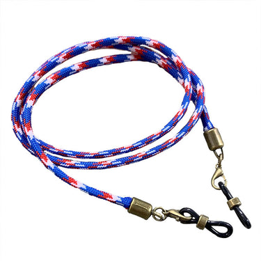 A loosely coiled Julbo Eyewear Vintage Sunglass Lanyard in braided blue, red, and white, featuring brass and black metal clips on each end. #color_vintage-sunglass-lanyard-patriot