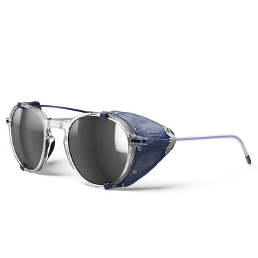 The Julbo Eyewear Legacy RX features clear vintage-inspired frames, dark or photochromic lenses, blue leather side shields, and thin metal arms, displayed against a white background. #color_crystal-/-blue