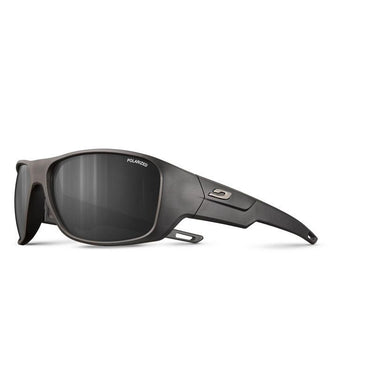 Julbo Eyewear’s Rookie 2 Kids sunglasses feature black polarized thick frames, dark lenses, and a small metallic logo on the arms. Engineered with Julbo sun technology for optimal protection, shown on a white background. #color_black-with-spectron-3-polarized-lens