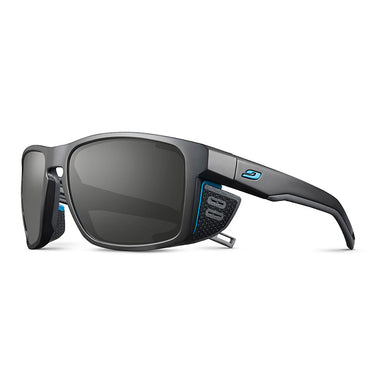 Julbo Eyewear Shield RX: Black sport sunglasses with rectangular lenses, side shields, and blue accents. Enjoy optical precision with REACTIV photochromic Rx lenses for the ultimate prescription sunglasses, shown on a white background. #color_black-/-blue
