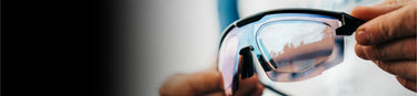Close-up of a person holding a pair of sports sunglasses with reflective lenses.