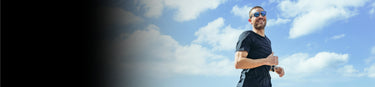 A man in a black shirt and sunglasses is jogging outdoors under a blue sky with scattered clouds.