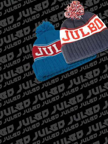 Two knit beanies with pom-poms, one blue and one gray, both with the word JULBO on the front, displayed on a background patterned with the word JULBO.