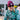 A woman wearing a green camouflage jacket, a maroon beanie with a visible Fetboi label, and black sunglasses, smiling outdoors near a fire pit.