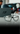 A pair of black-rimmed eyeglasses is displayed on a white surface with a branded box and blurred background objects behind them.