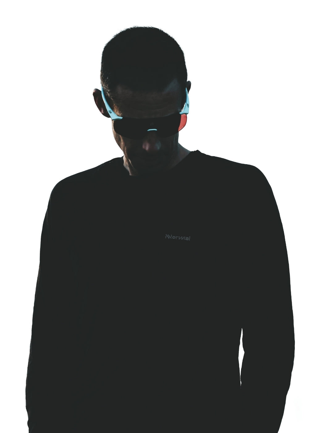 A person wearing sunglasses and a dark shirt stands against a white background, with their face partially shadowed and head slightly bowed.