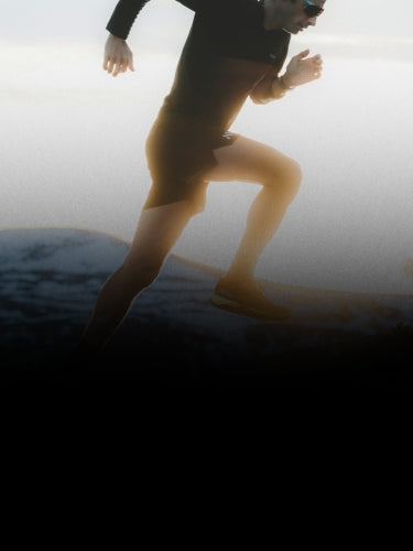 A person wearing sunglasses and athletic clothing runs outdoors, silhouetted against a bright sky and mountainous landscape.