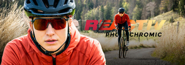 A cyclist wearing a red jacket, black helmet, and sunglasses is seen close up and riding a bike on a rural road with REACTIV PHOTOCHROMIC text in the background.
