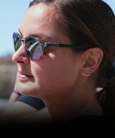 Woman wearing sunglasses looks into the distance outdoors on a sunny day.