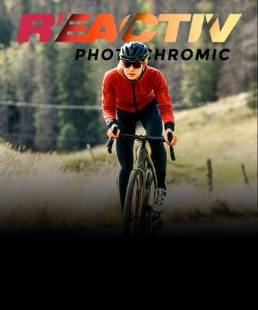 A cyclist wearing a red jacket and helmet rides a bike on a rural path with hills and trees in the background; REACTIV PHOTOCHROMIC text is overlaid.