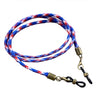 A loosely coiled Julbo Eyewear Vintage Sunglass Lanyard in braided blue, red, and white, featuring brass and black metal clips on each end. #color_vintage-sunglass-lanyard-patriot