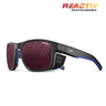 The Julbo-usa Shield sport sunglasses feature black and blue frames, red-tinted REACTIV PHOTOCHROMIC lenses, and side vents—ideal adventure eyewear for your next outdoor journey. #color_translucent-black-blue-white-with-reactiv-0-4-high-contrast-lens