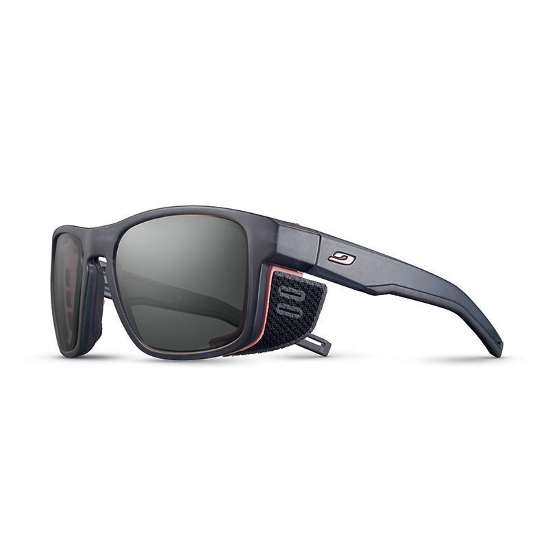 Julbo Eyewear's Shield M RX sports sunglasses feature a matte black frame with dark lenses, red accents, removable side shields, and a fabric temple strap. Compatible with REACTIV photochromic Rx lenses for custom prescriptions. #color_translucent-gray-/-pink
