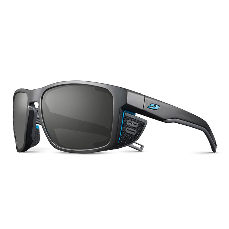 Julbo Eyewear Shield RX: Black sport sunglasses with rectangular lenses, side shields, and blue accents. Enjoy optical precision with REACTIV photochromic Rx lenses for the ultimate prescription sunglasses, shown on a white background. #color_black-/-blue